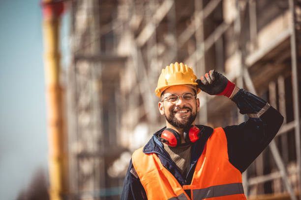 Construction site manager standing  wearing safety vest and helmet, thinking at construction site. Young architect watching construction site with confidence.